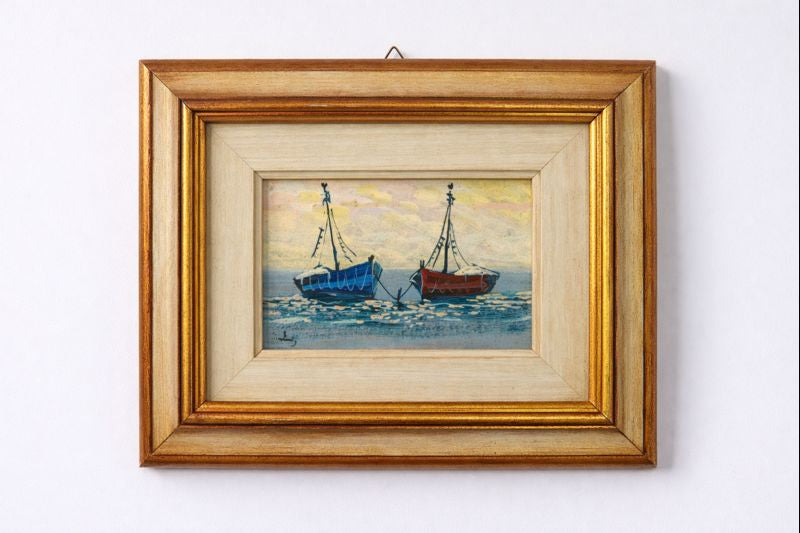 Framed painting of two boats on a white wall